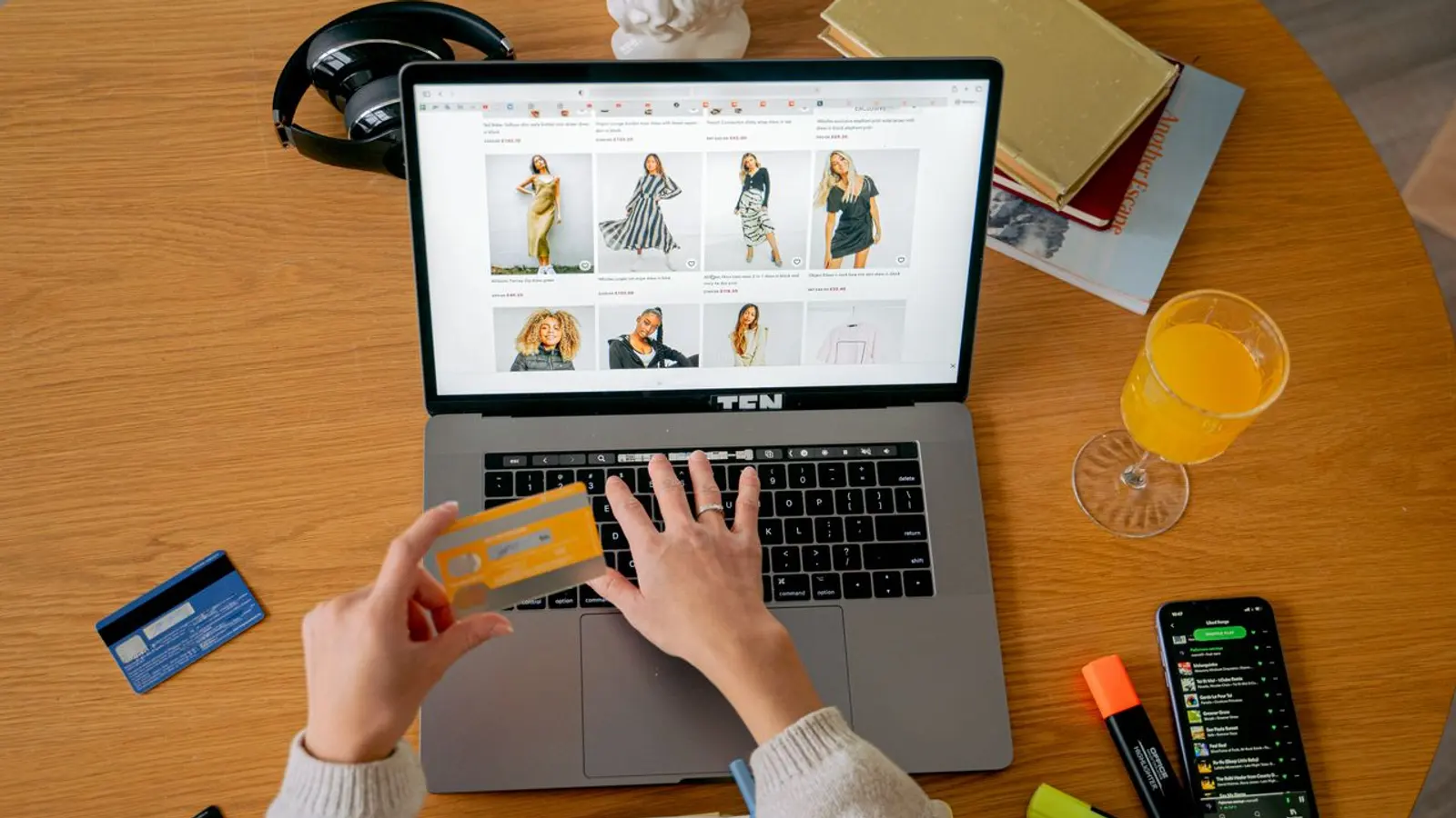 Manos con una tarjeta frente a una laptop que muestra una tienda de ropa.